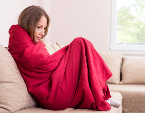 A woman wrapped up in a blanket considering calling Gas Doctor for Emergency Heating Service